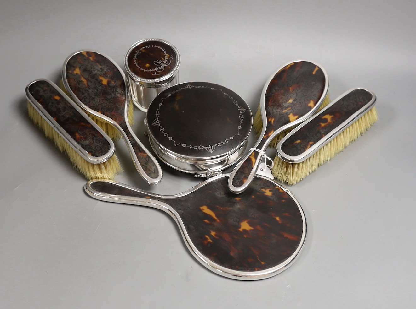 A matched George V seven piece silver and tortoiseshell pique mounted mirror, brush, toilet jar and trinket box set, marks rubbed, trinket box Birmingham, 1925, 12.4cm.